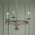 Silver 3-light crown chandelier with intricate metal scrollwork, hanging in front of a green paneled wall.