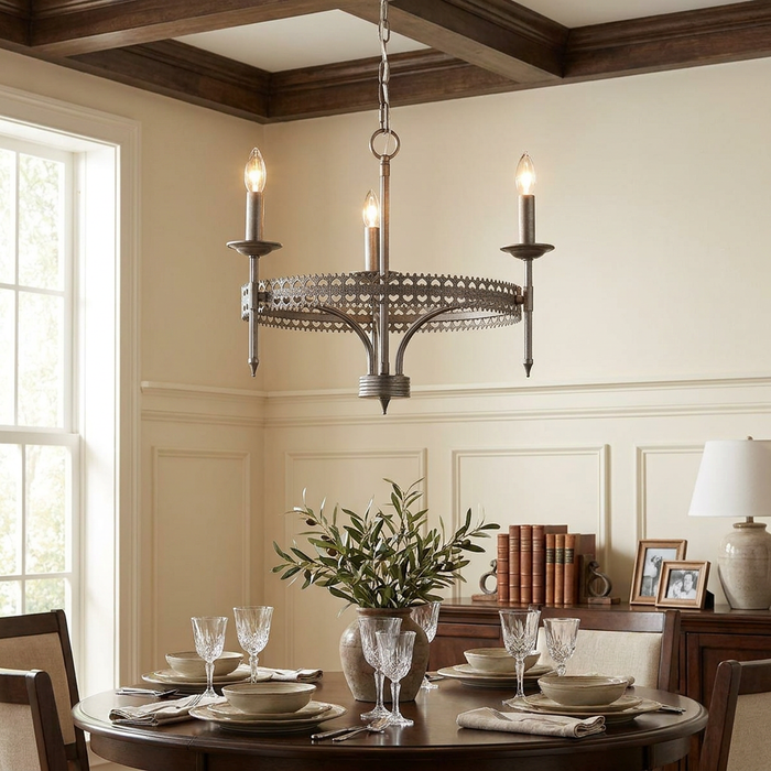 Silver three-light chandelier with a decorative crown band hanging over a dining table in a neutral-toned room.