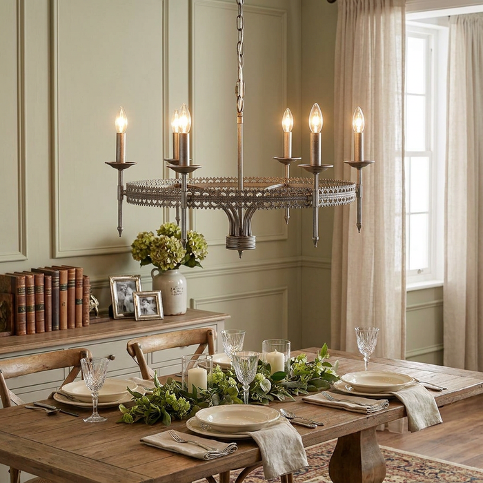 A silver crown chandelier with six candle lights hanging over a decorated wooden dining table in a rustic room.