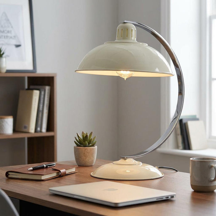 Cream dome desk lamp with a curved chrome arm on a wooden desk with a laptop and a succulent.