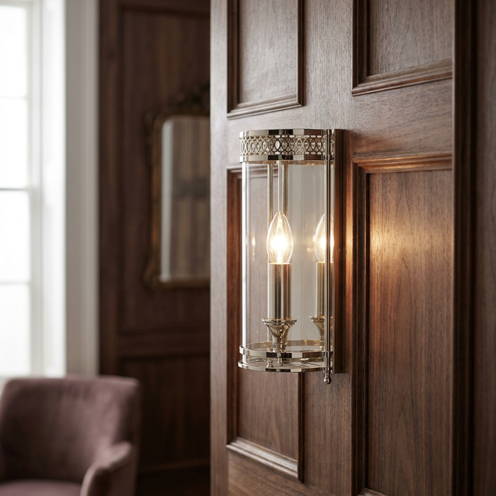 Elstead Guildhall nickel wall light with a clear glass cylinder and lit bulb on a wood-paneled wall.