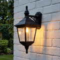 Black traditional carriage-style wall lantern glowing on a white brick exterior wall.