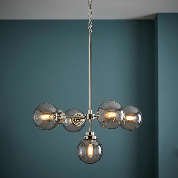 Modern 5-light chandelier with polished nickel frame and smoke glass globes against a dark blue wall.