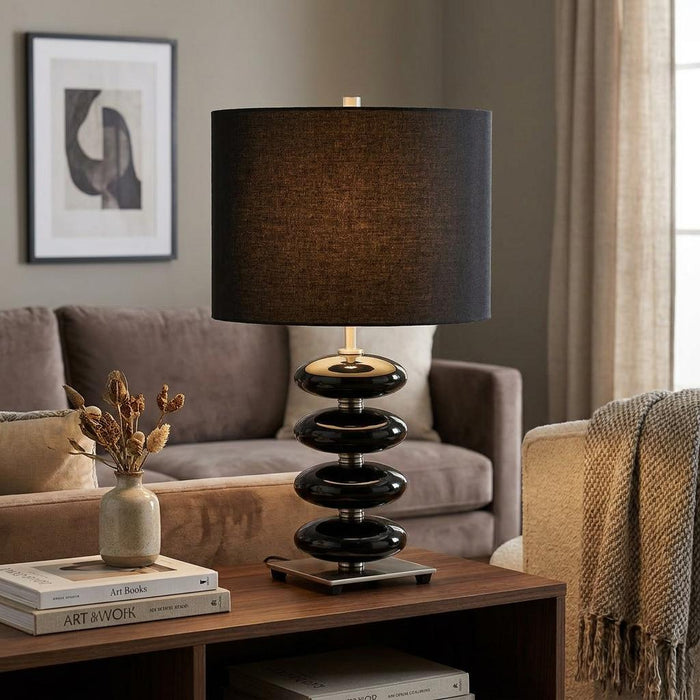 Black ceramic pebble-base table lamp with a dark fabric drum shade on a wooden side table in a modern living room.