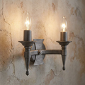Medieval-style two-light wall sconce with a hammered silver finish and glowing candle bulbs on a textured wall.