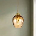 Amber swirl glass teardrop pendant light with brass fittings and a glowing bulb against a muted green wall.