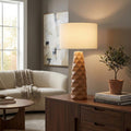 Caramel ceramic table lamp with a geometric base and drum shade on a wooden sideboard in a cozy living room.