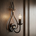 Rust and gold scroll wall sconce with a lit candle bulb, mounted on a dark wooden wall.
