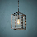 Gunmetal lantern-style pendant light with horizontal glass slats and a glowing bulb against a textured blue wall.