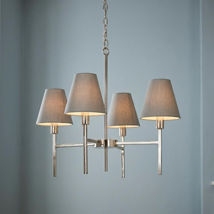 Modern four-light brushed nickel chandelier with grey fabric tapered shades against a soft blue wall.