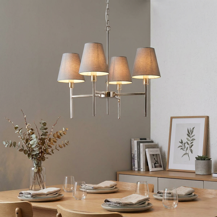 A four-light brushed nickel chandelier with grey fabric shades hanging above a modern dining room table.