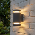 Elstead Magnus 2 light grey outdoor wall light with a warm glow, mounted on a white brick wall.