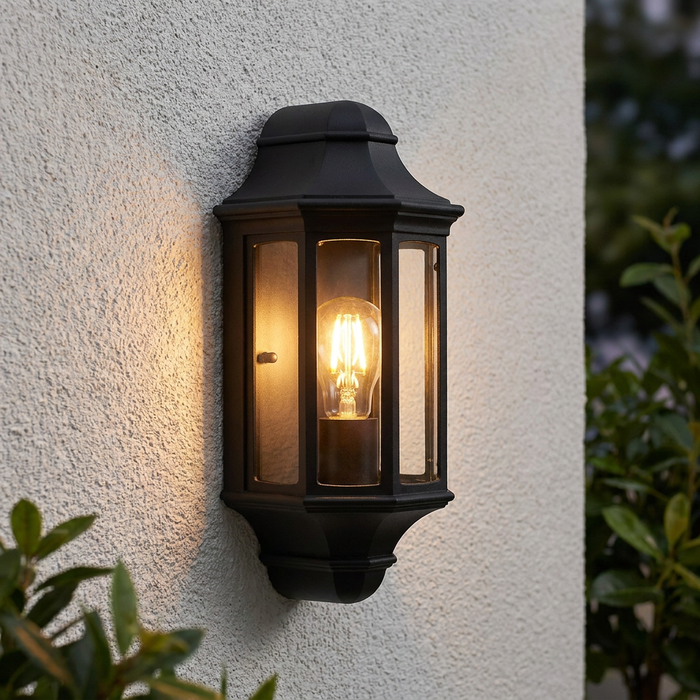 Elstead Malaga black mini outdoor half wall lantern with an illuminated bulb on a textured white wall.