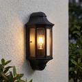 Elstead Malaga black mini outdoor half wall lantern with an illuminated bulb on a textured white wall.