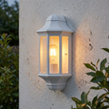 White lantern wall light with a glowing filament bulb mounted on an exterior textured wall.