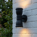 Black outdoor up and down wall light mounted on a white brick wall, casting warm light upwards and downwards.