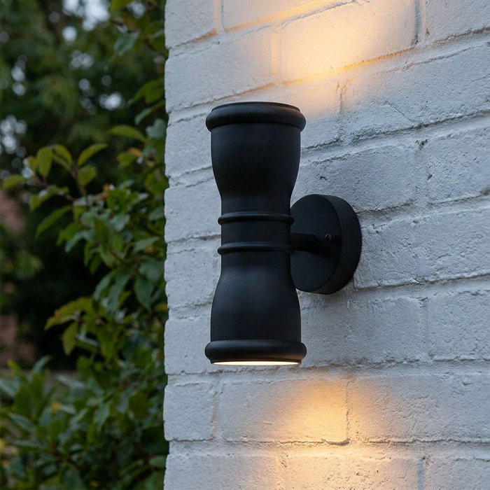 Black outdoor up and down wall light mounted on a white brick wall, casting warm light upwards and downwards.