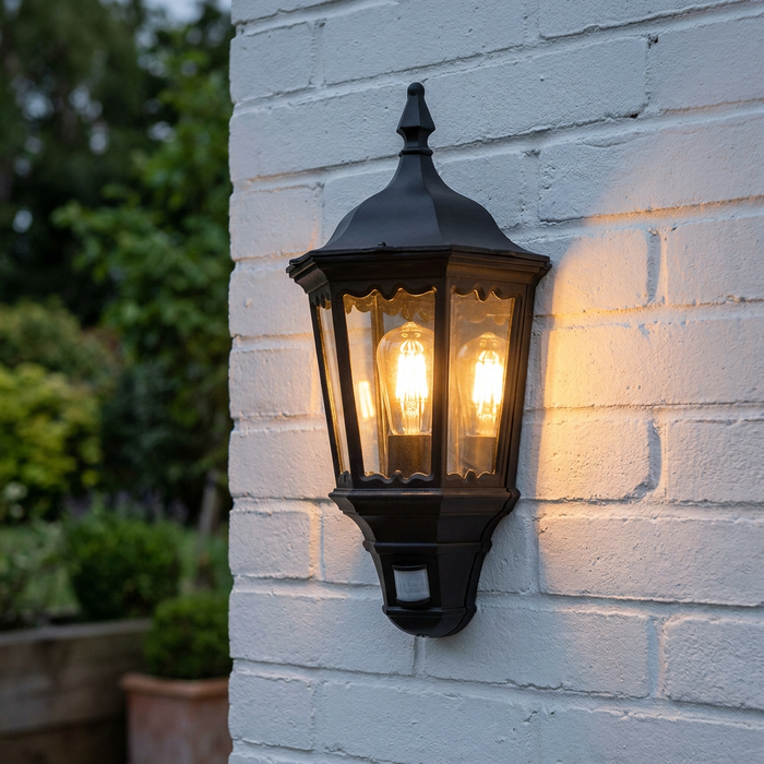 Traditional black lantern wall light with a glowing filament bulb and motion sensor on a white brick wall.