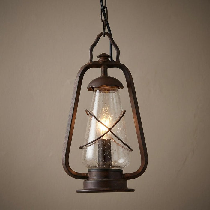 Rustic old bronze lantern pendant light with seeded glass and a warm glowing bulb.