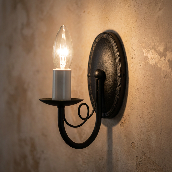 Black candle-style wall sconce with a scrolled arm and glowing bulb mounted on a textured beige wall.