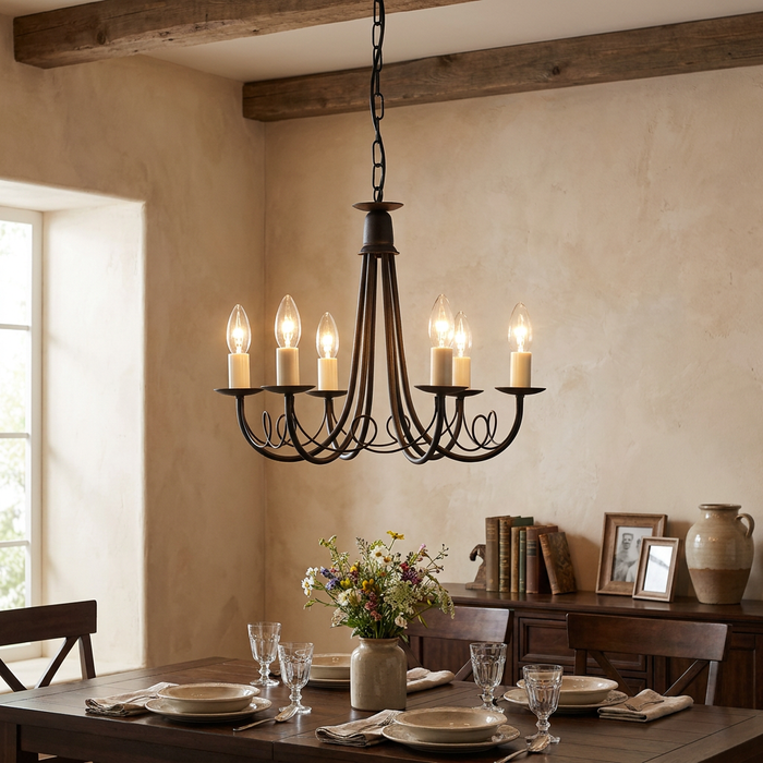 A black six-light chandelier with candle bulbs and scrolled metal arms hanging over a rustic wooden dining table.