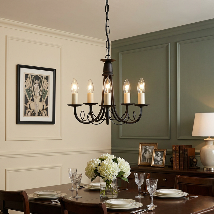 A five-light black and gold chandelier with elegant scrollwork hanging over a dining table in a classic interior.
