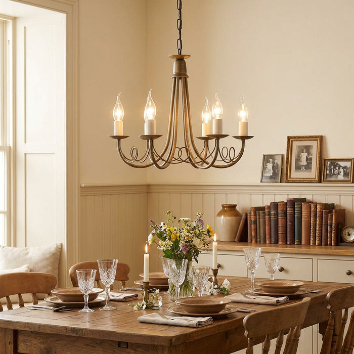 Black and gold 6-light chandelier with scrolled metal arms hanging over a rustic dining table set for a meal.