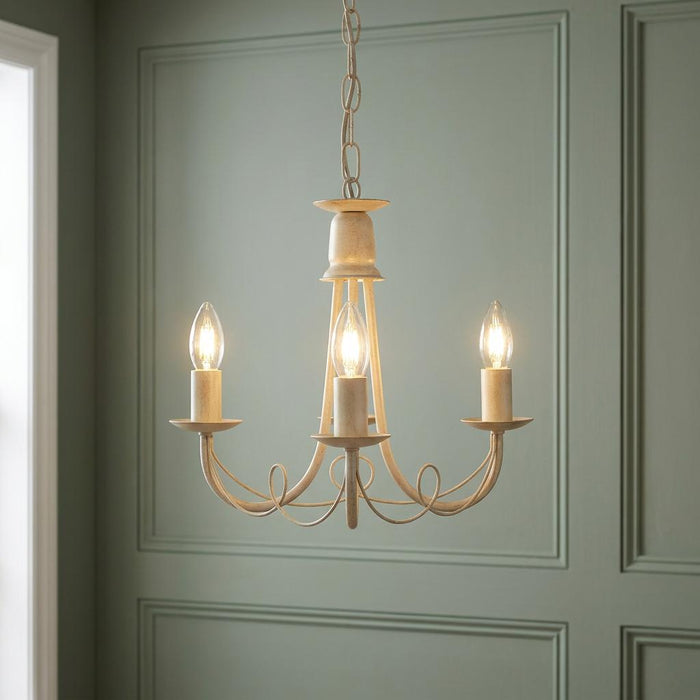 Three-light ivory and gold chandelier with candle bulbs illuminated against a green paneled wall.