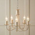 Five-light ivory and gold chandelier with decorative scrolled arms and candle-style bulbs against a paneled wall.