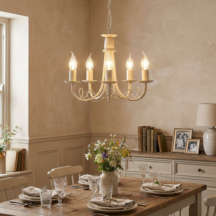 Ivory and gold 5-light scroll chandelier hanging in a rustic dining room above a set wooden table.