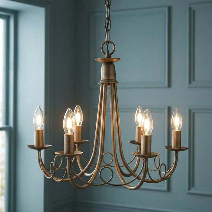 Elstead Minster 6-light ivory and gold chandelier with lit candle bulbs against a blue paneled wall.