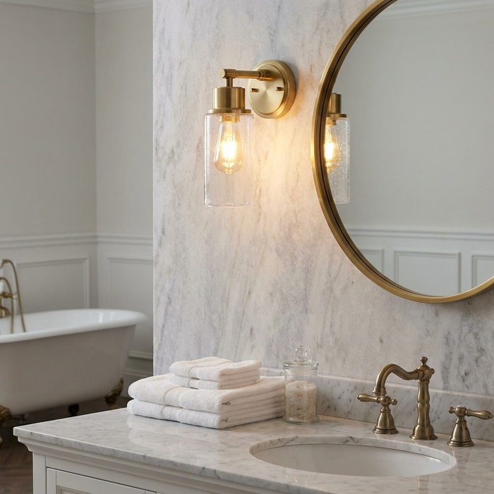 Elstead Morvah brushed brass wall light with seeded glass on a marble wall next to a mirror in a luxury bathroom.