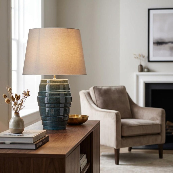 Blue tiered ceramic table lamp with a beige shade on a wooden sideboard in a cozy living room.