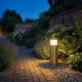 An Elstead New Brighton brass outdoor bollard light illuminating a brick garden path at twilight.