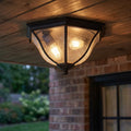 Traditional bronze flush-mount outdoor ceiling light with seeded glass, mounted on a wooden porch ceiling.