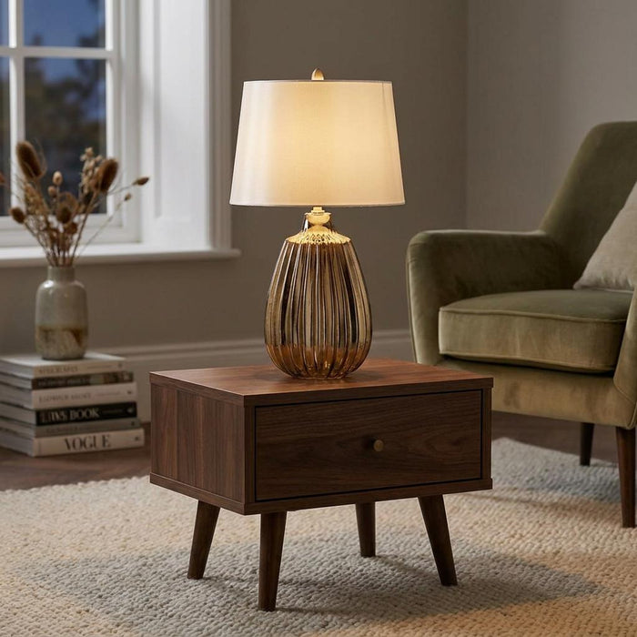 Small bronze ceramic table lamp with a ribbed base and cream shade on a wooden side table in a living room.