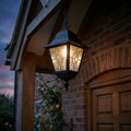 Black Elstead Norfolk pendant lantern with diamond-leaded glass hanging from a wooden porch at twilight.
