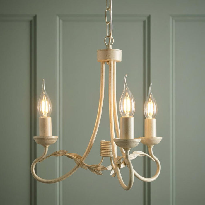 Ivory and gold three-light chandelier with decorative leaf accents hanging against a sage green paneled wall.