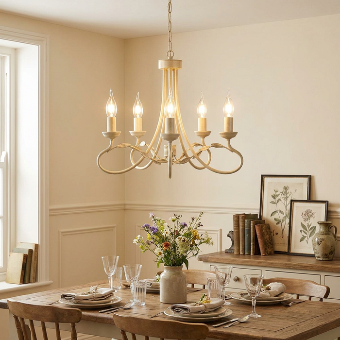Ivory and gold five-light chandelier with leaf scrolls hanging above a set dining table in a rustic room.