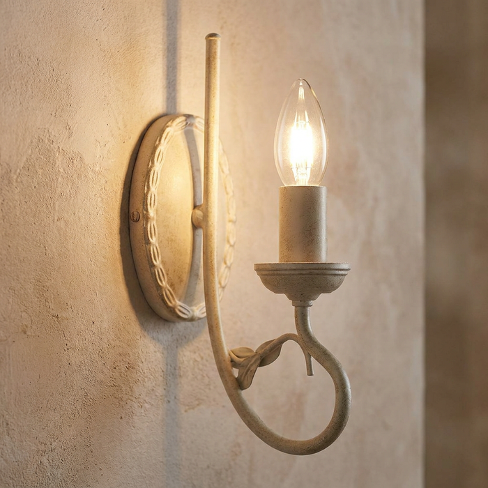 Ivory and gold candle-style wall light with a decorative backplate and curved arm on a textured wall.