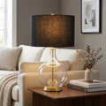 Table lamp featuring a clear glass orb base, brass accents, and a black fabric shade on a wooden side table.