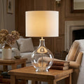 Elstead Orb Clear Table Lamp with a cream shade on a wooden side table in a cozy living room.