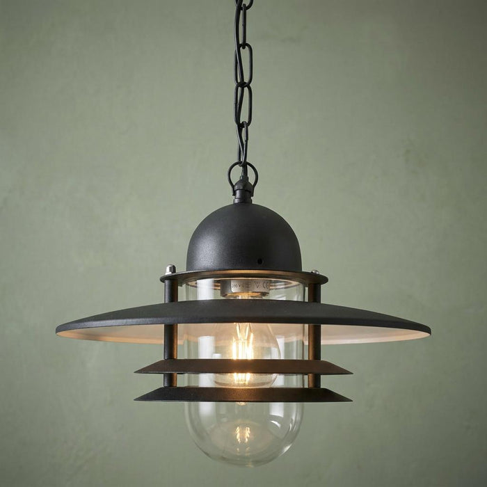 Black outdoor pendant light with tiered metal rings and a clear glass cylinder hanging from a chain.