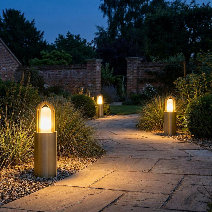 Brass bollard light with a warm glowing opal glass diffuser illuminating a stone garden path at night.