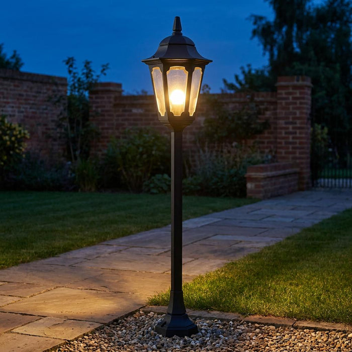 Classic black Elstead Parish outdoor bollard light illuminating a garden pathway at twilight.