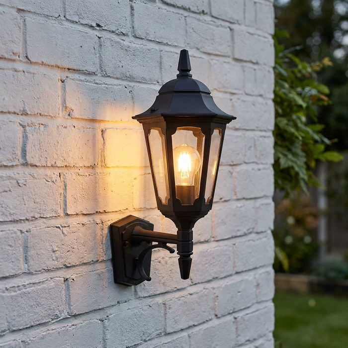 A black traditional outdoor wall lantern illuminated against a white brick wall.