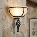 Elstead Pembroke black wall uplighter with a twisted metal frame and glowing frosted glass shade on a rustic wall.