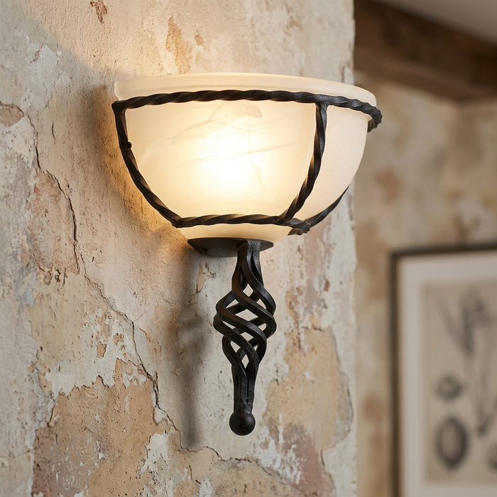 Elstead Pembroke black wall uplighter with a twisted metal frame and glowing frosted glass shade on a rustic wall.