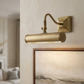 A brushed brass picture light mounted on a wall, illuminating a framed landscape painting.