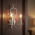 A two-light chrome wall sconce with candle-style bulbs and a crystal droplet mounted on a dark wood panel.